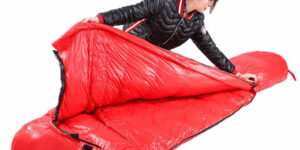 an image of a woman showing a red sleeping bag interior and exteriors by half opening it.